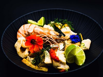 Hotel in Ötztal: restful sleep Gourmet shrimp dish with lime wedges and edible flowers in a black bowl