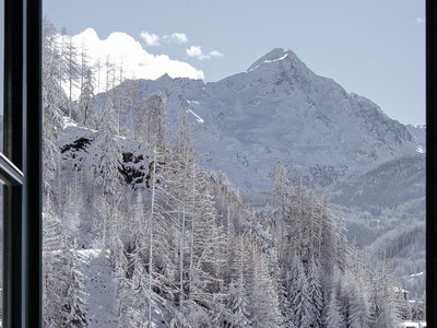 Hotel in Sölden mit 4-Sterne-Service Blick durch eine offene Balkontür auf verschneite Berge und Tannenbäume