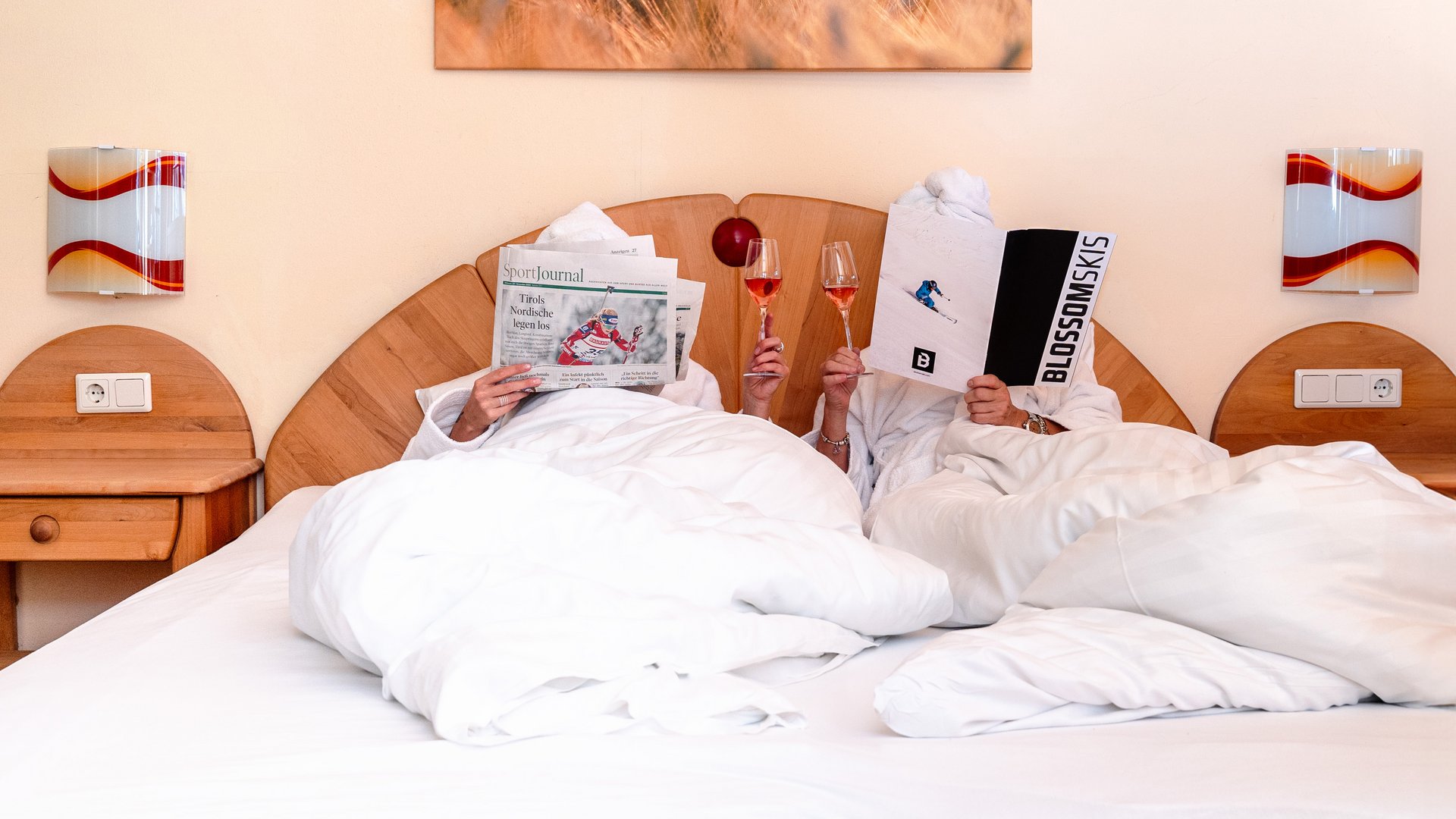 Hotel im Ötztal: erholsamer Schlaf Zwei Personen lesen im Bett Zeitung und trinken Wein