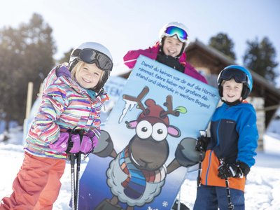 Sunny holiday in Sölden, Austria Three smiling children with skis and helmets standing by a cartoon reindeer sign in the snow