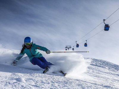 Looking for excursion destinations in Sölden? Skier in blue gear skiing on fresh snow with cable cars in the background