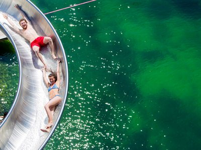 Freizeitarena Sölden und noch viel mehr Zwei Personen rutschen an einer Wasserrutsche in einen See und halten Händchen