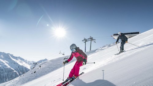 Dein 4-Sterne-Hotel im Ötztal Zwei Skifahrer fahren bei sonnigem Wetter den schneebedeckten Hang hinunter