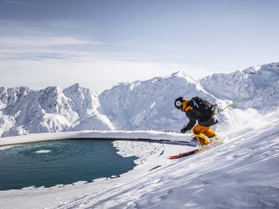 Looking for excursion destinations in Sölden? Skier descending snowy slope beside a circular partially frozen water reservoir in the mountains