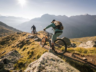 Looking for excursion destinations in Sölden? Two mountain bikers riding a trail down a sunny alpine mountain ridge