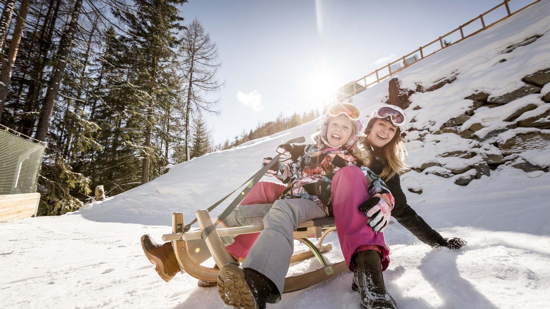 Looking for excursion destinations in Sölden? Woman and child smiling while sledding in the snow on a sunny winter day