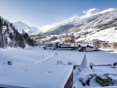 Hotel in Sölden mit 4-Sterne-Service Verschneites Bergdorf mit Häusern und schneebedeckten Alpen im Hintergrund