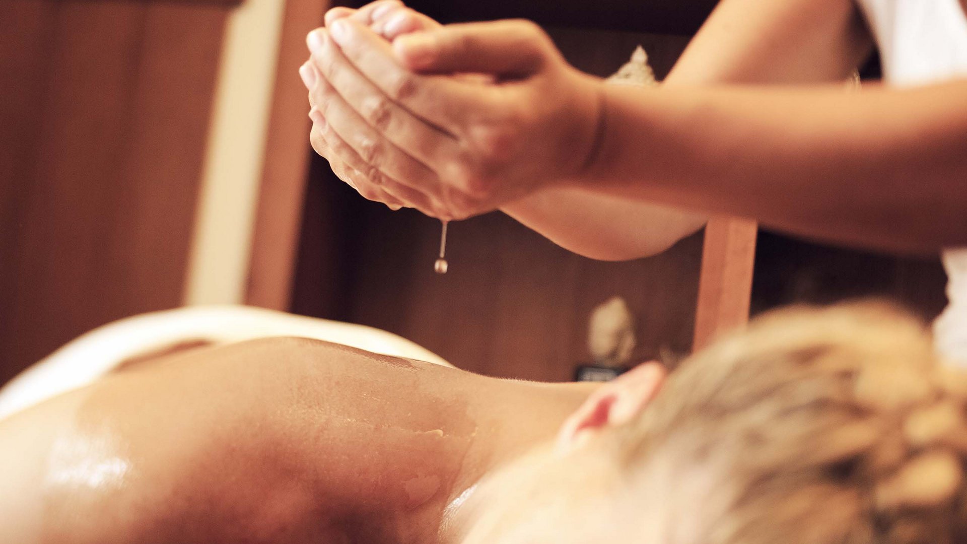 Wellnesshotel in Sölden: Hotel Sunny Person empfängt Massage mit Öl, Hände lassen Öl auf den Rücken tropfen