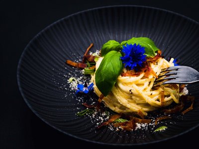 Das Restaurant in Sölden im Hotel Sunny Spaghetti mit Speck, Basilikum und blauer Blüte auf schwarzem Teller