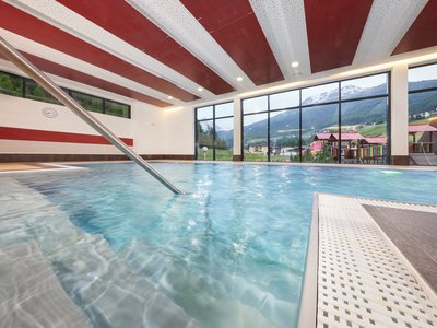 Wellnesshotel in Sölden: Hotel Sunny Hallenbad mit Bergblick und farbenfrohem Spielplatz vor großen Fenstern