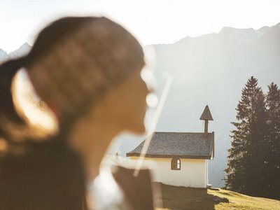 Hotel in Sölden mit 4-Sterne-Service Unscharfe Person im Vordergrund vor einer kleinen Kapelle und Berglandschaft