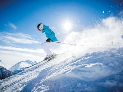 Holiday in Sölden: what’s included Skier in blue jacket skiing down a snowy slope with sun and mountains