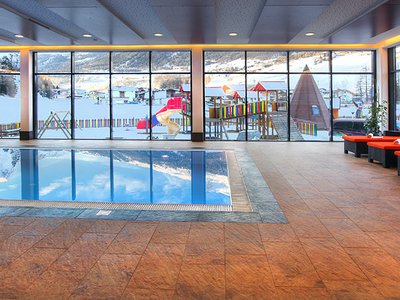Wellness hotel in Sölden: Hotel Sunny Indoor pool with red lounge chairs and snowy playground visible outside