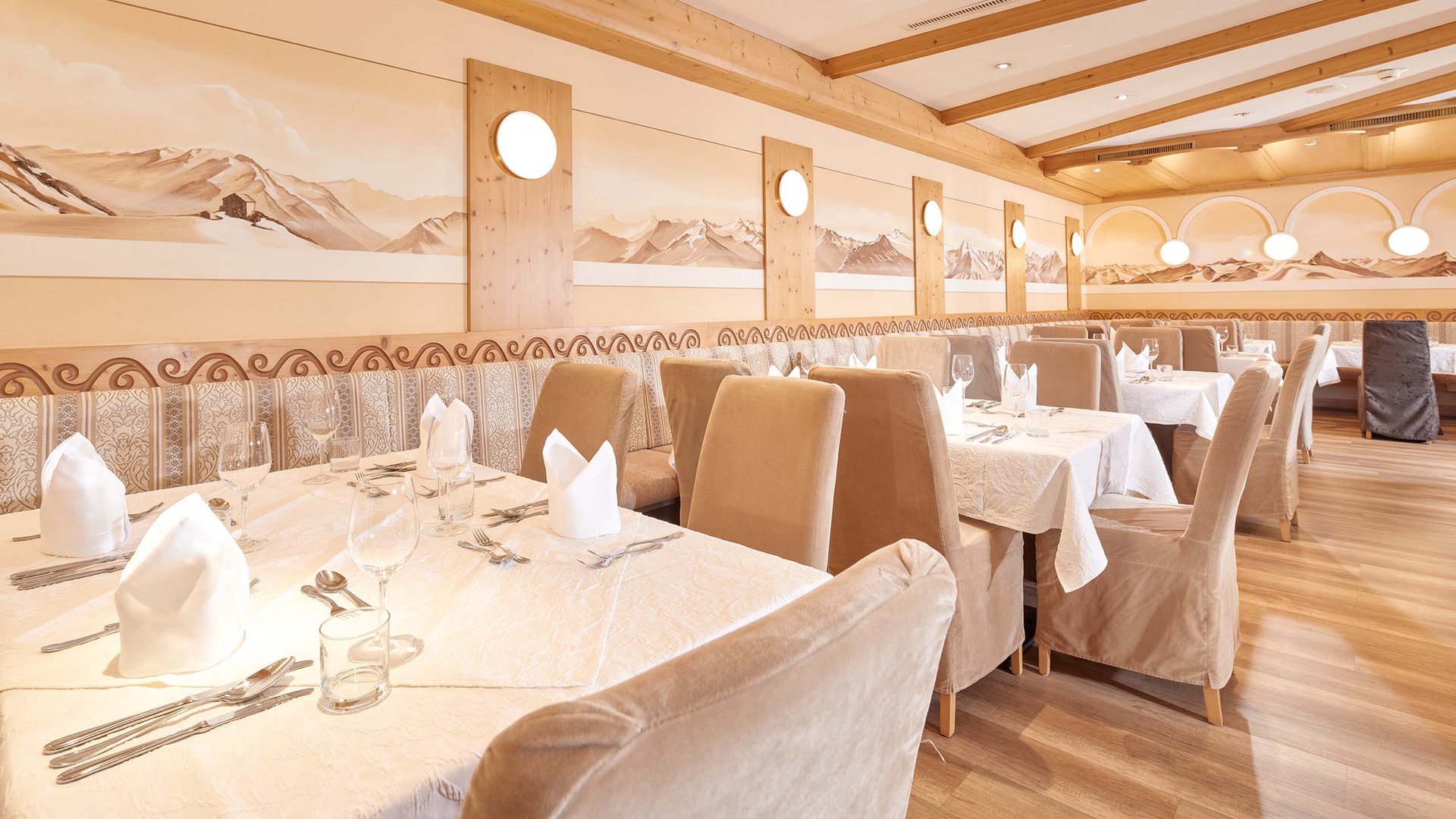 Dein 4-Sterne-Hotel im Ötztal Heller Speisesaal mit gedeckten Tischen und Berglandschaft an den Wänden