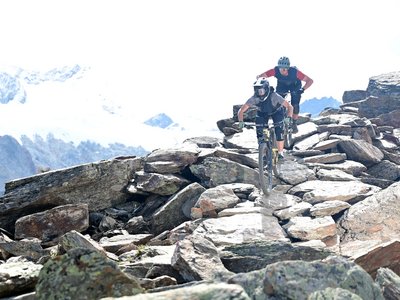 Sunny holiday in Sölden, Austria Two mountain bikers ride across rocky terrain against an alpine mountain backdrop