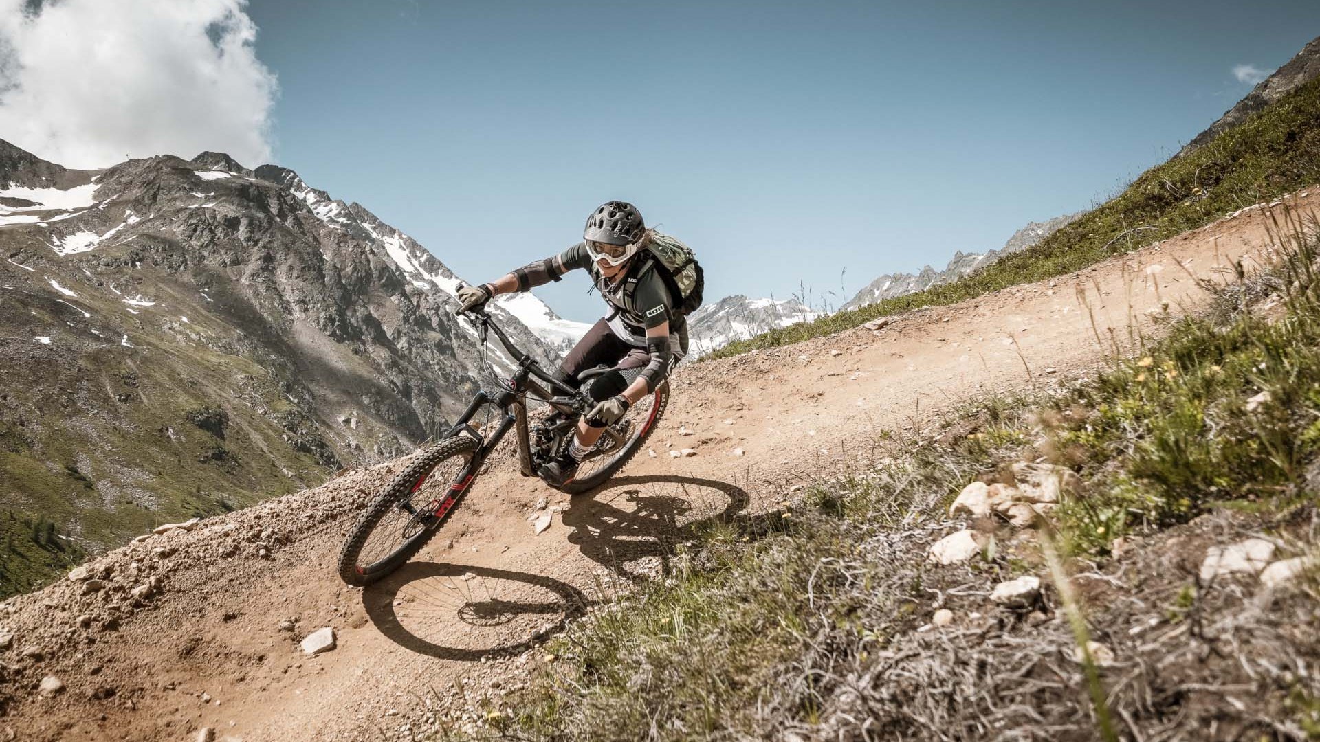 Ausflugsziele in Sölden gesucht? Mountainbiker fährt auf kurvigen, bergigen Pfad bei klarem Himmel