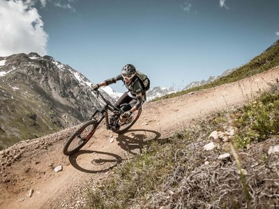Dein 4-Sterne-Hotel im Ötztal Mountainbiker fährt auf kurvigen, bergigen Pfad bei klarem Himmel