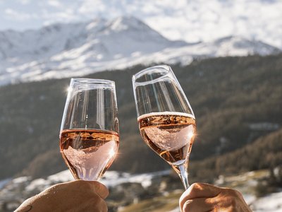 Hotel in Sölden mit 4-Sterne-Service Zwei Personen stoßen auf einem Balkon mit Sektgläsern vor verschneiter Bergkulisse an
