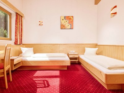 Familienhotel in Sölden: Hotel Sunny Sölden Zweibettzimmer mit roten Teppich, Holzmöbeln und Sonnenlicht am Fenster